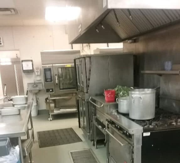 Empty restaurant kitchen with clean stoves, fryers, and ceiling with
